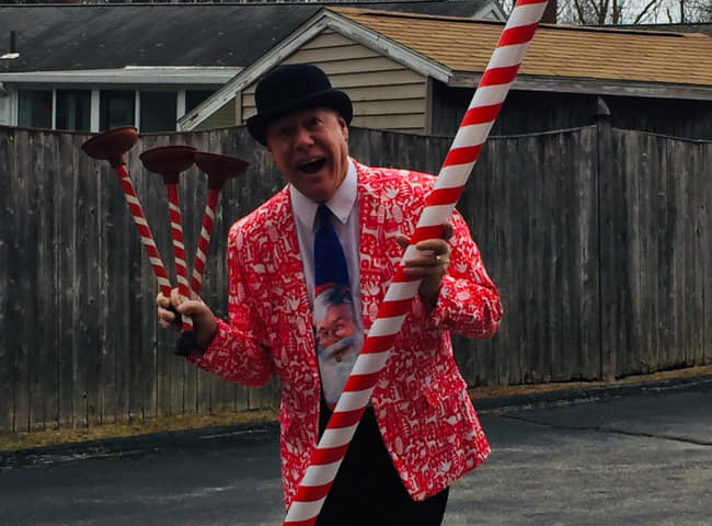 Flippo wearing a Santa themes suit and tie holding a jiant candy cane and candy cane plungers